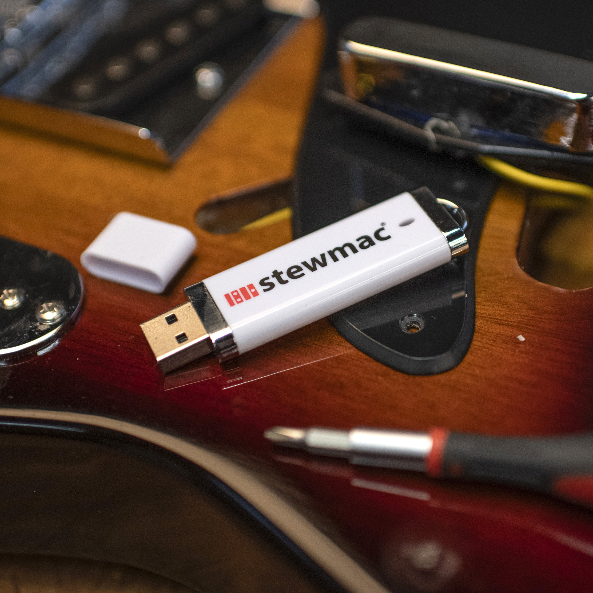 Une clé USB contenant des vidéos StewMac posée sur une guitare avec des outils de lutherie.